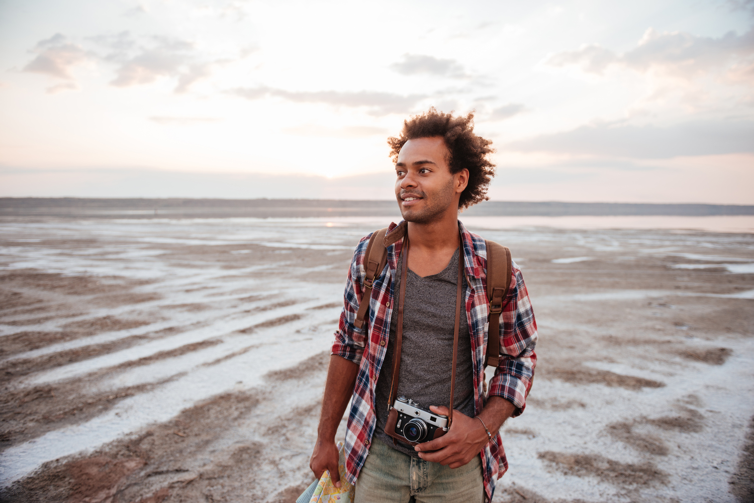 Happy man with backpack and vintage camera walking on beach - Tennis Destination
