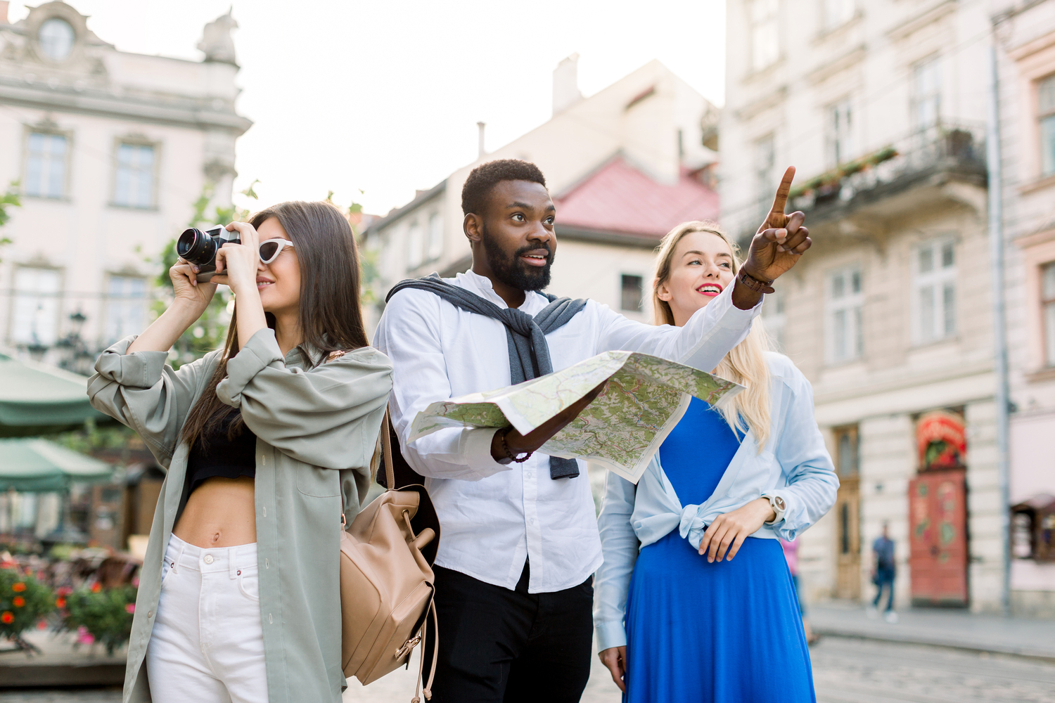 Multi-ethnic travelers using local map together on sunny day, African man pointing forward and showing something to blond girl. Pretty brunette Caucasian woman makes photos on her camera - Tennis Destination