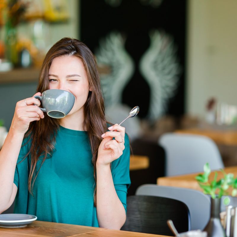 Beautiful elegant girl having breakfast at outdoor cafe. Happy young urban woman drinking coffee